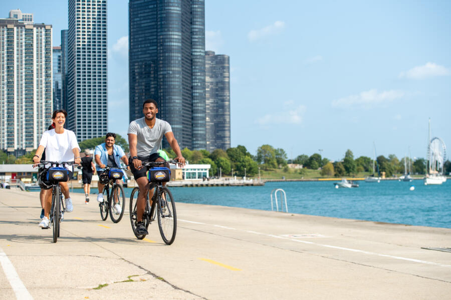 A group of friends bike down the pier near Lake Michigan with tall Chicago buildings in the background.