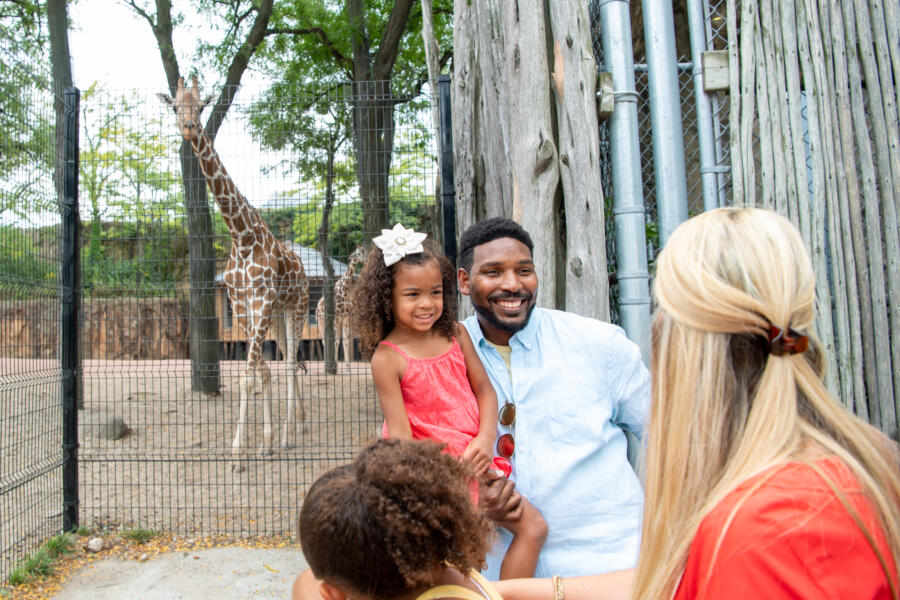 Father and daughter take picture in front of a Giraffe at the Lincoln Park Zoo.