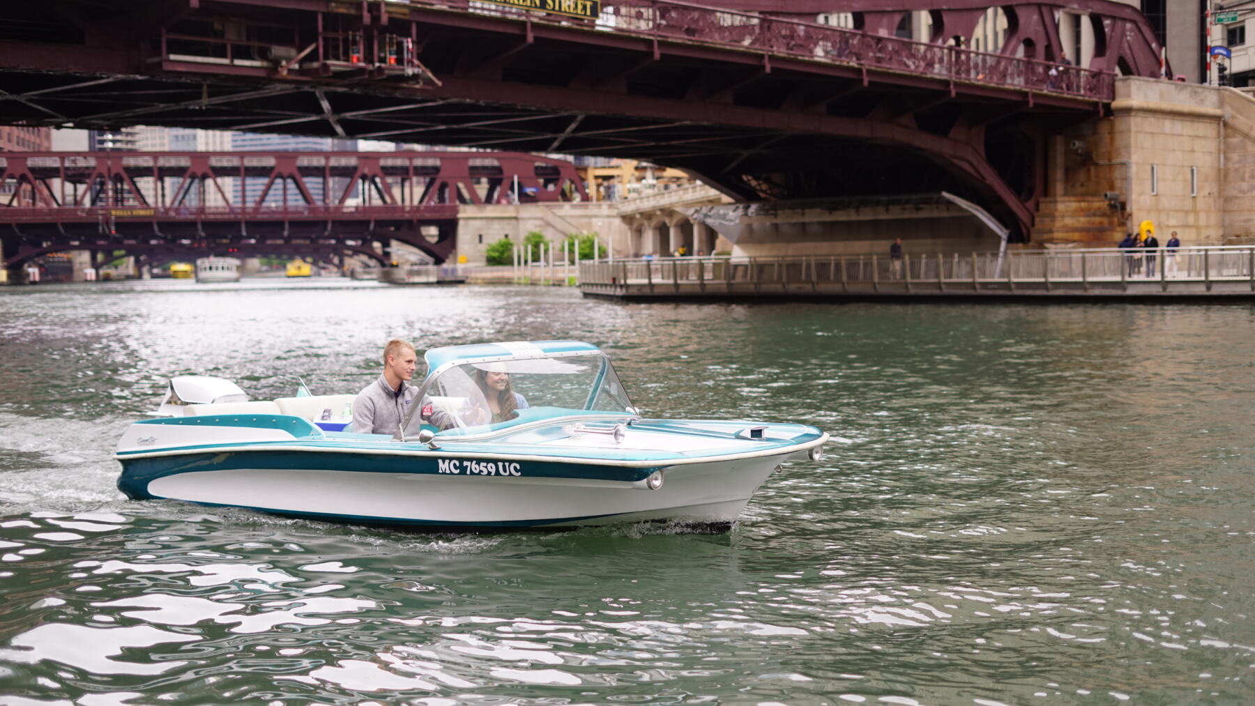 A retro-designed boat glides across the Chicago River underneath a bridge.