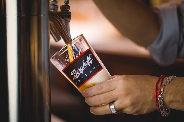Berghoff Bartender Pours Beer At an Angle With Foam Filling Up the Top.